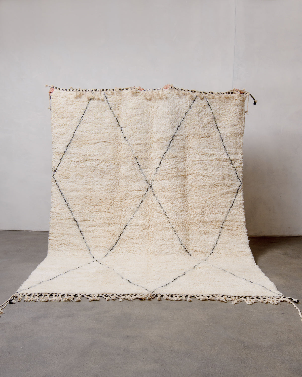 Cream Berber rug with black diamond design being held up in front of white wall.